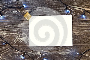 Horizontal paper blank with christmas lights frame. Flat lay. New year card gift. Gold presents. On grey wooden background. Top