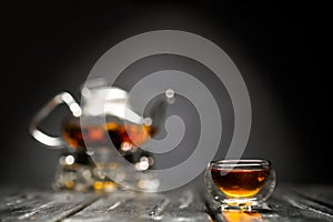 Horizontal photo of the tea set on a black background. Glass transparent teapot and cup. Black leaf tea.