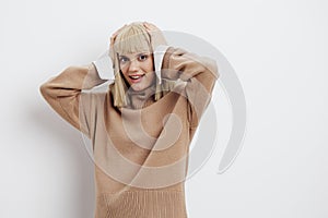 Horizontal photo, a woman on a white background in a beige sweater with beautiful blond hair smiles looking at us with