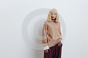 Horizontal photo, a woman on a white background in a beige sweater and brown trousers with beautiful blond hair is