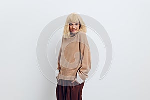 Horizontal photo, a woman on a white background in a beige sweater and brown trousers with fine blond hair stands and