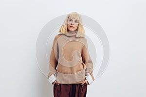 Horizontal photo, a woman on a white background in a beige sweater and brown trousers with fine blonde hair stands