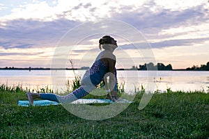 Horizontal photo of a young woman doing yoga by the river at sunset
