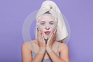 Horizontal picture of good looking magnetic female putting hands on face, having face mask, caring about skin, doing beauty