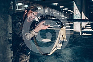 Horizontal picture of soldier is sitting on the ground on one knee near column and screaming. He is taking aim. Guy is