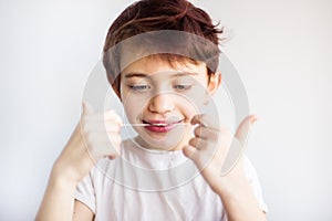 Horizontal portrait of 7 years old smiling child in white t-shirt looking on dental floss for teeth on white background isolated.