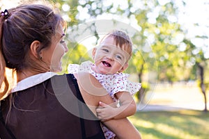 Horizontal portrait against the background of nature of a cheerful one-year-old baby in her motherâ€™s arms