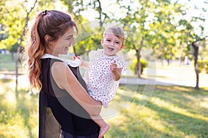 Horizontal portrait against the background of nature of a laughing one-year-old baby in her motherâ€™s arms