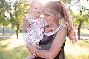 Horizontal portrait against a nature background of a cheerful twenty five year old woman with one year old daughter in her arms