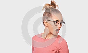 Horizontal portrait of amazed beautiful young woman wearing pink blouse with mouth opened posing over white studio background.