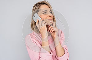 Horizontal portrait of beautiful pensive Caucasian blonde female has phone conversation, talk using modern cellphone, wears pink