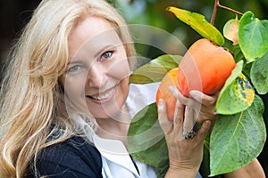 Horizontal portrait of Caucasian blond woman picking hachiya persimmons