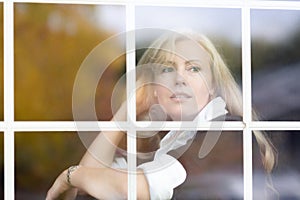 A horizontal portrait of Caucasian woman with long blond hair behind a window glass, dreamy