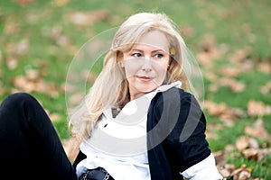 A horizontal portrait of Caucasian woman with long blond hair sitting on green grass  looking to her left