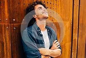 Horizontal portrait of cheerful young man with curly hair, smiling and looking up, feeling joyful, standing at modern metal