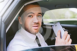 Horizontal portrait of a handsome Caucasian serious businessman calling on smart phone looking out the open car window