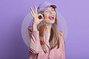 Horizontal portrait of magnetic pretty attractive female standing isolated over lilac background in studio, closing one eye,