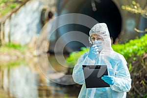 horizontal portrait of a scientist next to a sewer pipe with a walkie-talkie