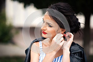 Horizontal portrait of young beautiful brunette woman with red lipstick touching her earring and looking away. Stylish girl in