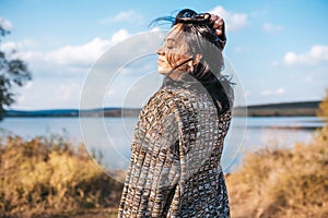 Horizontal rear view of beautiful female with blowing hair relaxing and enjoying nature next to the lake outdoors. Caucasian