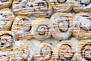 Horizontal rows of cinnamon buns in pan drizzled with vanilla frosting