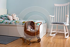 Horizontal selective focus view of toys in wicker stroller with white rocking chair and bed