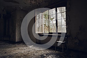 Horizontal shot of an abandoned room with an open window and a chair n front of it