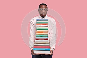 Horizontal shot of African American student has puzzled expression, surprised look, holds thick encyclopedia and