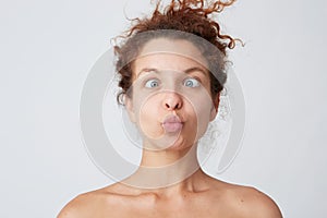 Horizontal shot of amuzing crazy young woman with curly hair and perfect skin making funny face and joking  over white
