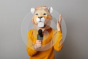 Horizontal shot of angry unknown man journalist wearing lion mask and orange jumper making reportage, telling something to
