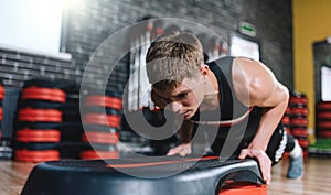 Horizontal shot of athlete man doing on stepper pushups in aerobic fitness club. The handsome male is exercising his chest on the