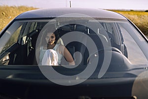 Horizontal shot of a beautiful young caucasian female posing in the front seat of a car in a field
