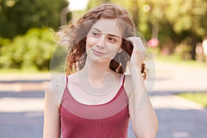 Horizontal shot of beautiful young woman having rest at park on summer day, . foxy haired female looking aside with dreamy facial