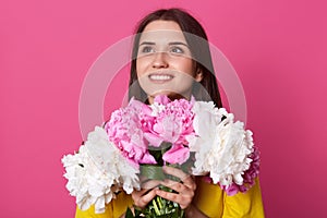 Horizontal shot of beautiful young woman with natural make up and long brunette hair holding pink and rose peony flowers, dreamy