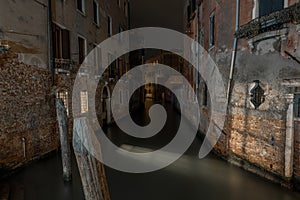 Horizontal shot of a canal between ancient apartment buildings in Venice, Italy at night time