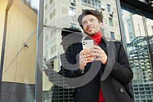 Horizontal shot of cheerful young handsome dark haired unshaved man looking gladly ahead while holding smartphone in raised hands