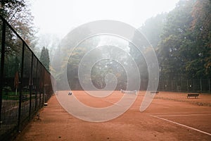 Horizontal shot of an empty tennis court in the forest in fog. The tennis player is hitting the ball