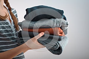 Horizontal shot of a Girl teenager with two braids holding a pile of clothes, isolated on gray background