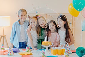 Horizontal shot of group of little children gather together to celebrate birthday, embrace and pose at camera, prepare for special