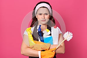 Horizontal shot of indignated stressed maid standing isolated over pink background in studio, having unpleasant facial expression