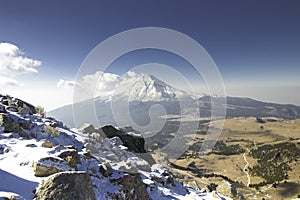 Horizontal shot of a landscape full of snow and rocks with an active volcano in the background in the mountains of Mexico