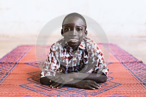 Horizontal Shot of Little African Schoolboy Lying Indoors Smiling for the Camera in village near Bamako, Mali