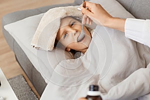 Horizontal shot of little unhealthy girl lying on cough, mother taking care of her sick daughter, giving her medicine, female kid