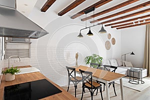 Horizontal shot of a loft-style kitchen-living room with a white wall of wooden beams with modern appliances, a dining