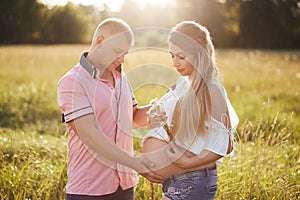 Horizontal shot of lovely friendly family anticipate for baby, stand outdoor, have stroll across summer field. Attractive male hol