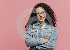 Horizontal shot of mirthful pleasant looking female model wears optical glasses and jean jacket, keeps arms folded over chest,