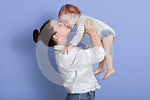 Horizontal shot of mom throws baby and kiss his, playing together and having fun, mother wearing white shirt and jeans, infant