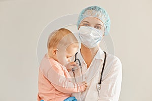 Horizontal shot of optimistic young adult female pediatrist wearing medical uniform, holding infant baby girl, examining child`s