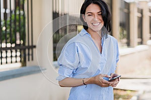 Horizontal shot of positive woman in blue shirt having happy expression. Elegant lady posing outdoors in park while having rest,