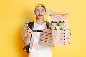 Horizontal shot of serious calm man courier with thermo backpack in white T-shirt and cap, looking at camera, holding client`s